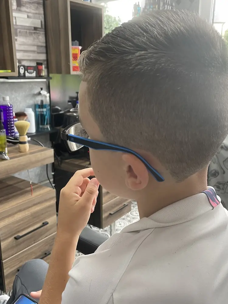 A boy in glasses sitting in the barber chair beside the shop window after his haircut